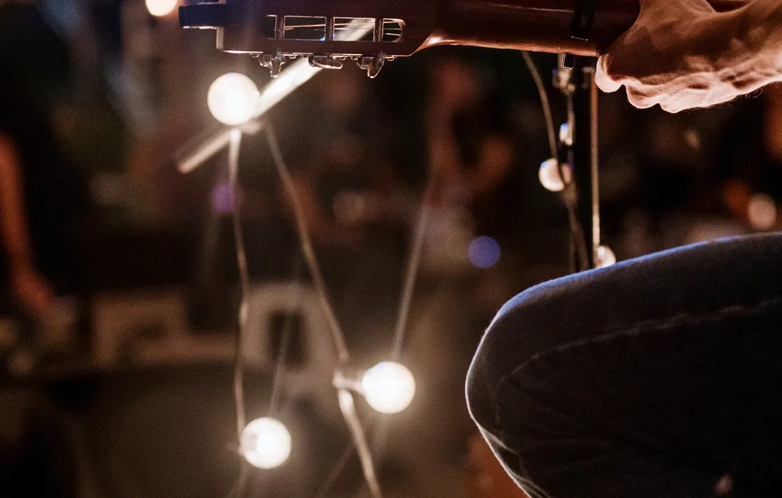 Person playing a guitar in front of a microphone, with their hand on the guitar and a blurred background